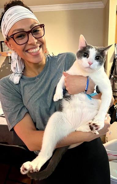 White female in a gray t-shirt, wearing glasses and a head band holding a large domestic cat